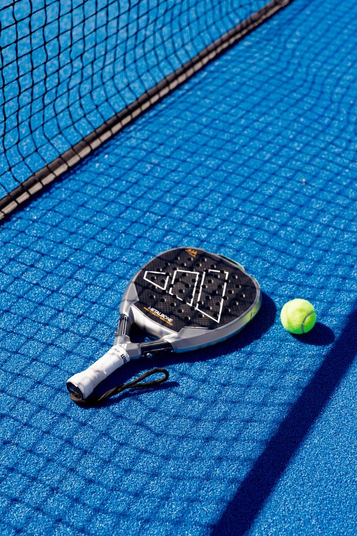 A padel racket and ball on a blue court