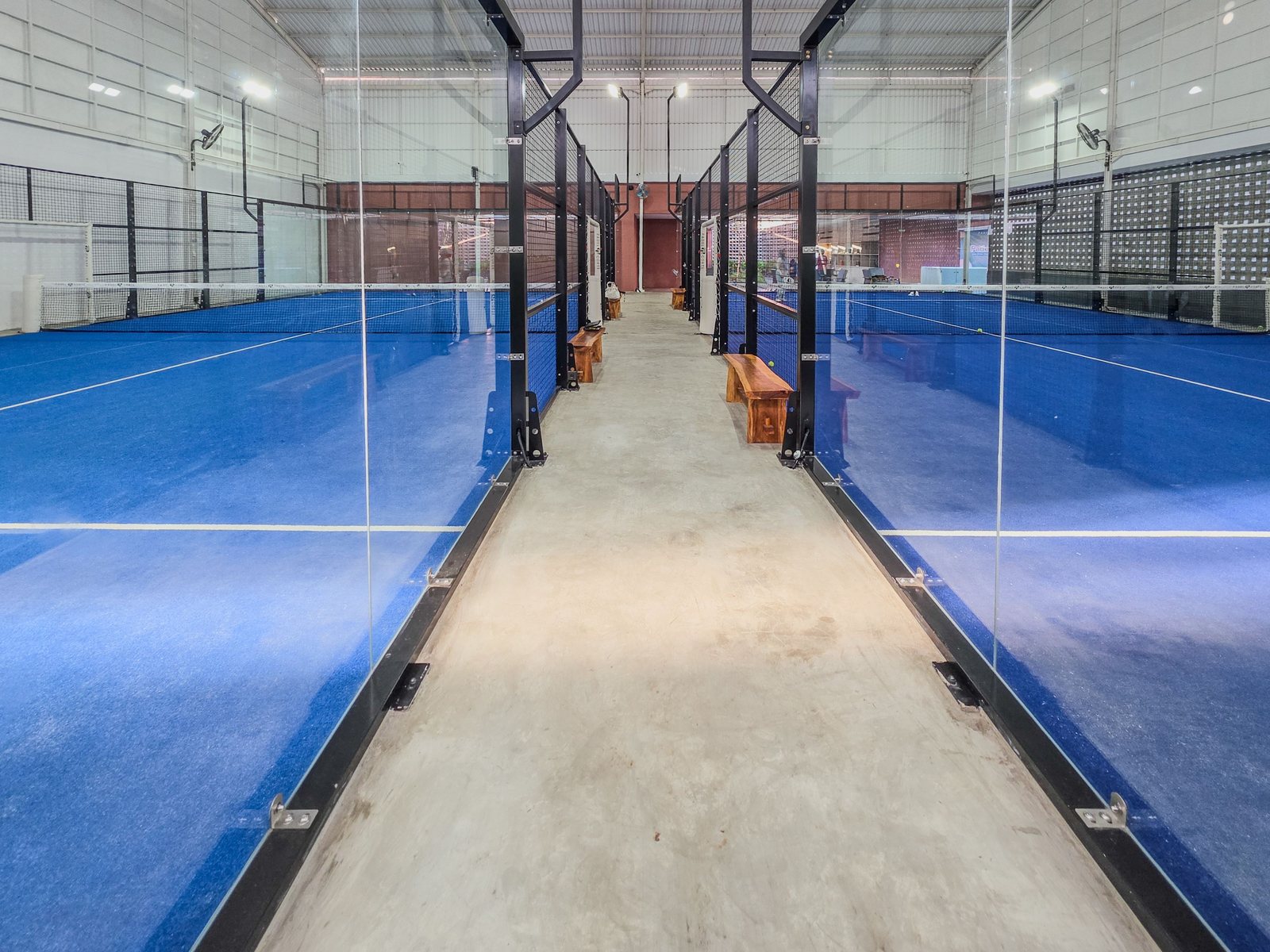 Indoor padel facility with bright blue courts behind panoramic glass walls